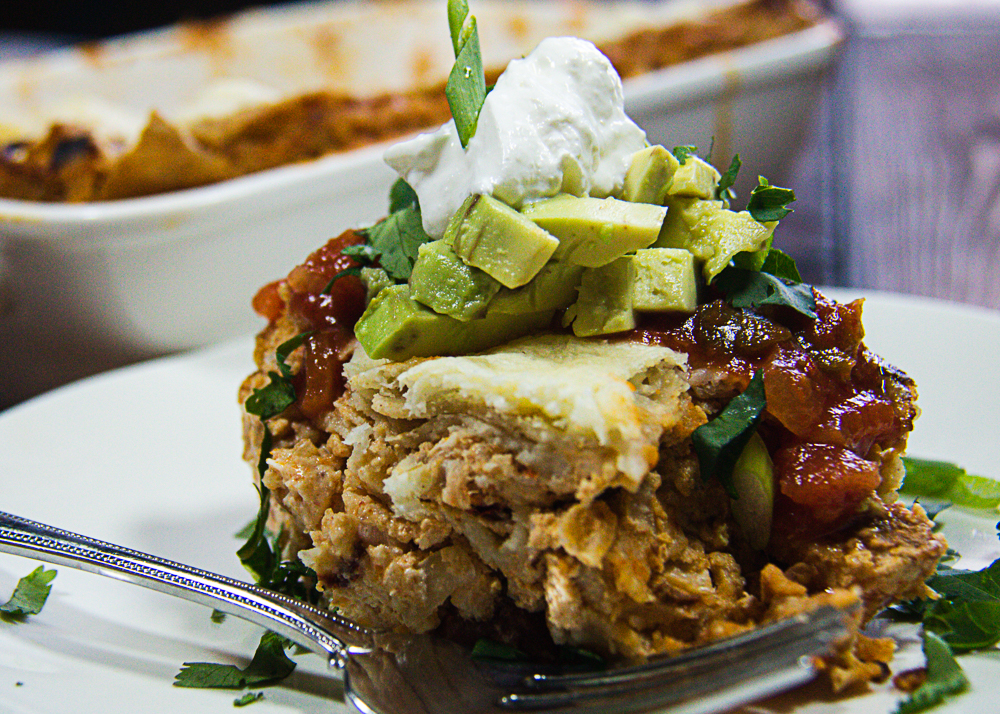 Chipotle chicken Mexican lasagna on plate with avocado and sour cream.