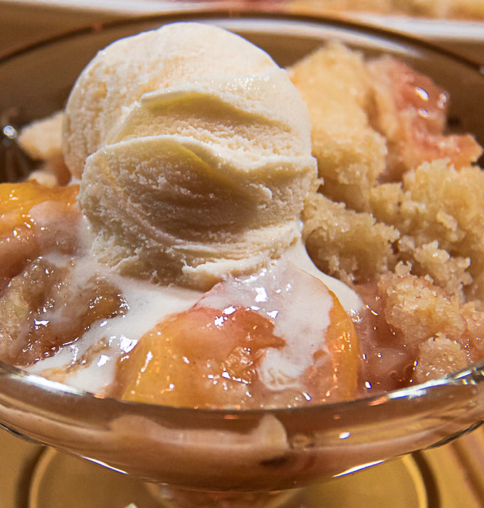 fresh peach crisp in a glass dish with ice cream