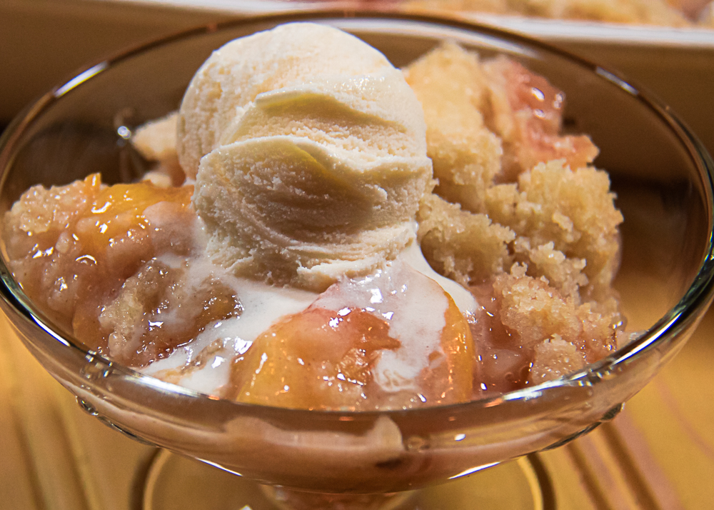 fresh peach crisp in a glass dish with ice cream